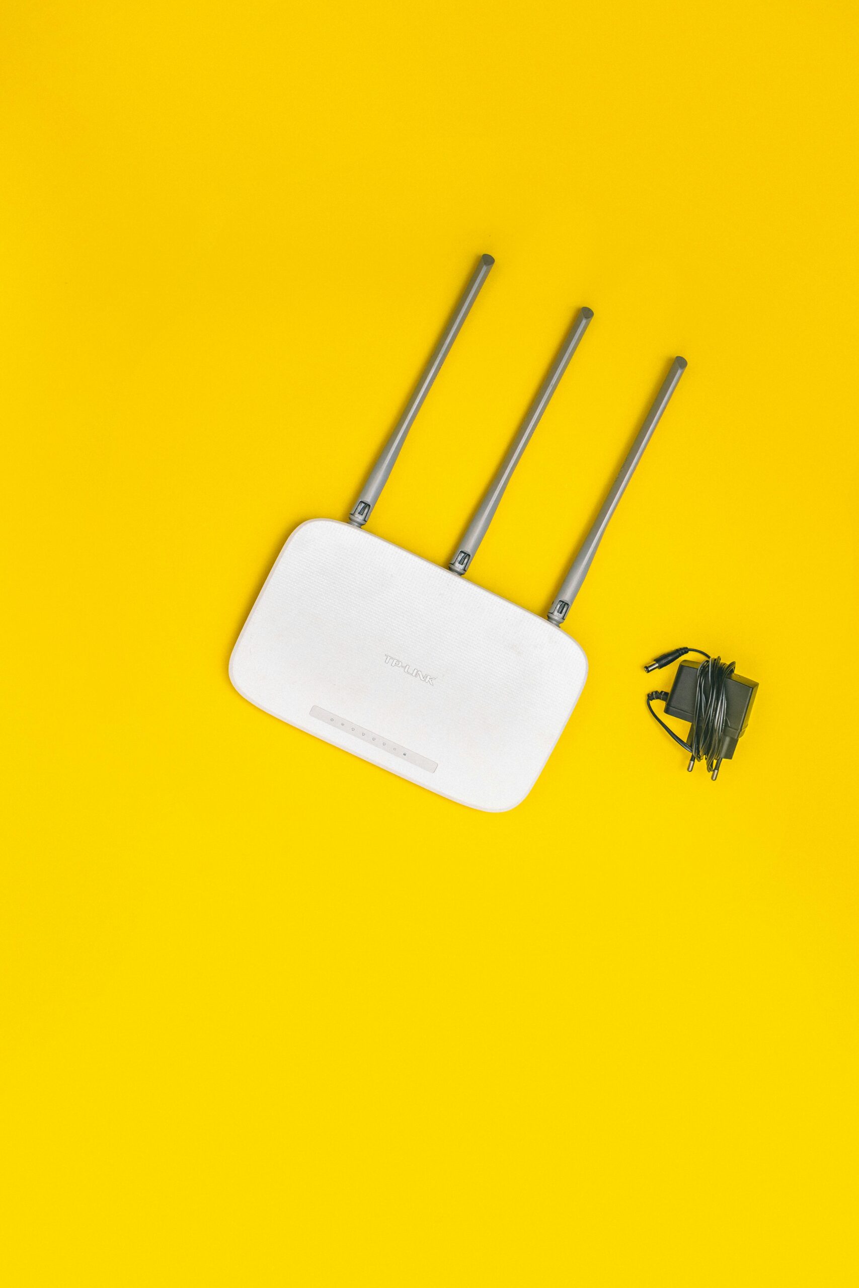 White wireless router with three antennas and a power adapter on a yellow background